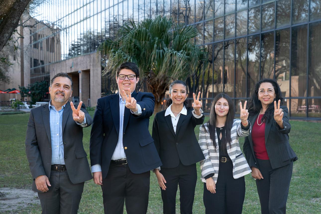 Students and professors standing outside in front of building holding v's up