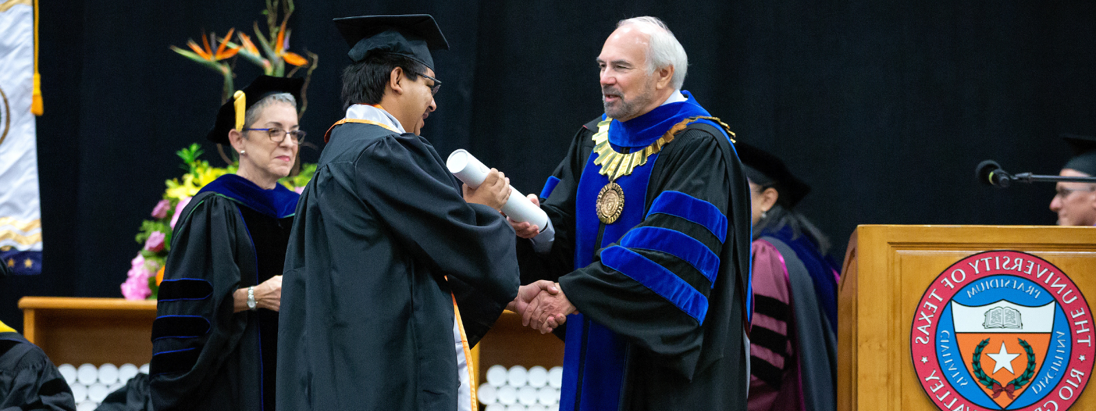 President Bailey presents a white diploma case to a student during the graduation commencement ceremony.